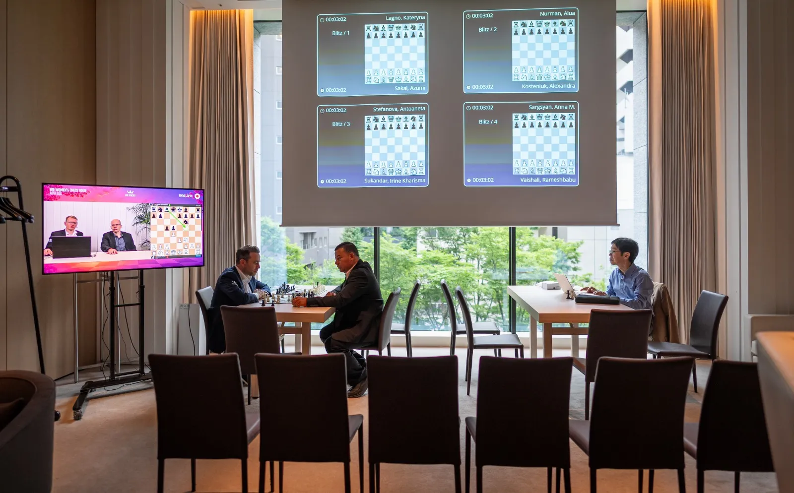 Behind the scenes at the Tokyo Toranomon Edition Hotel: all four quarterfinal games projected on screen, the WR Chess English broadcast running on the side monitor, and Wadim Rosenstein (left) at a board between rounds. Behind the scenes at the Tokyo Toranomon Edition Hotel: all four quarterfinal games projected on screen, the WR Chess English broadcast running on the side monitor, and Wadim Rosenstein (left) at a board between rounds.