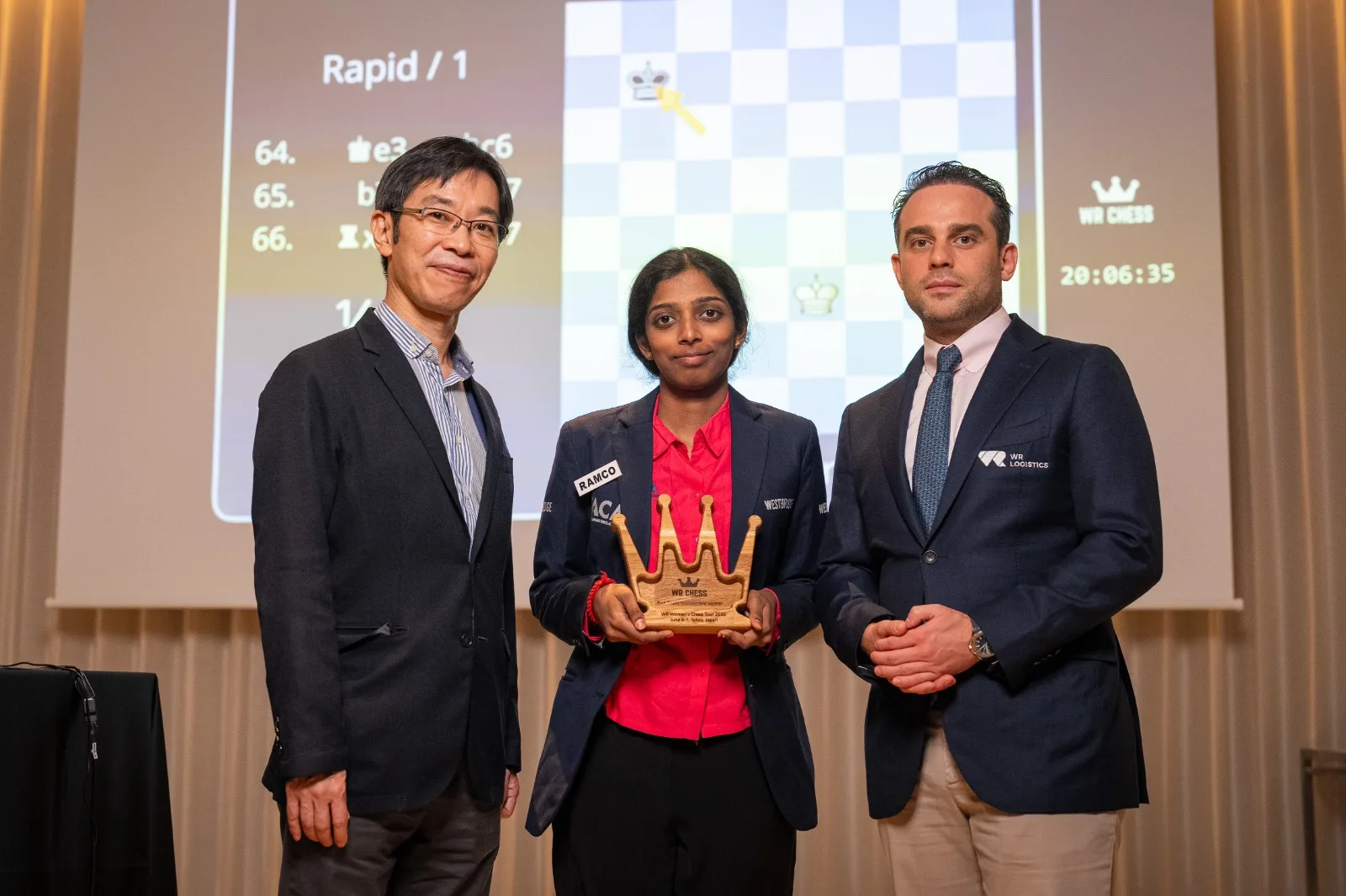 Vaishali Rameshbabu with the WR Chess crown after winning the Tokyo Rapid, flanked by Hiroshi Manabe and Wadim Rosenstein.